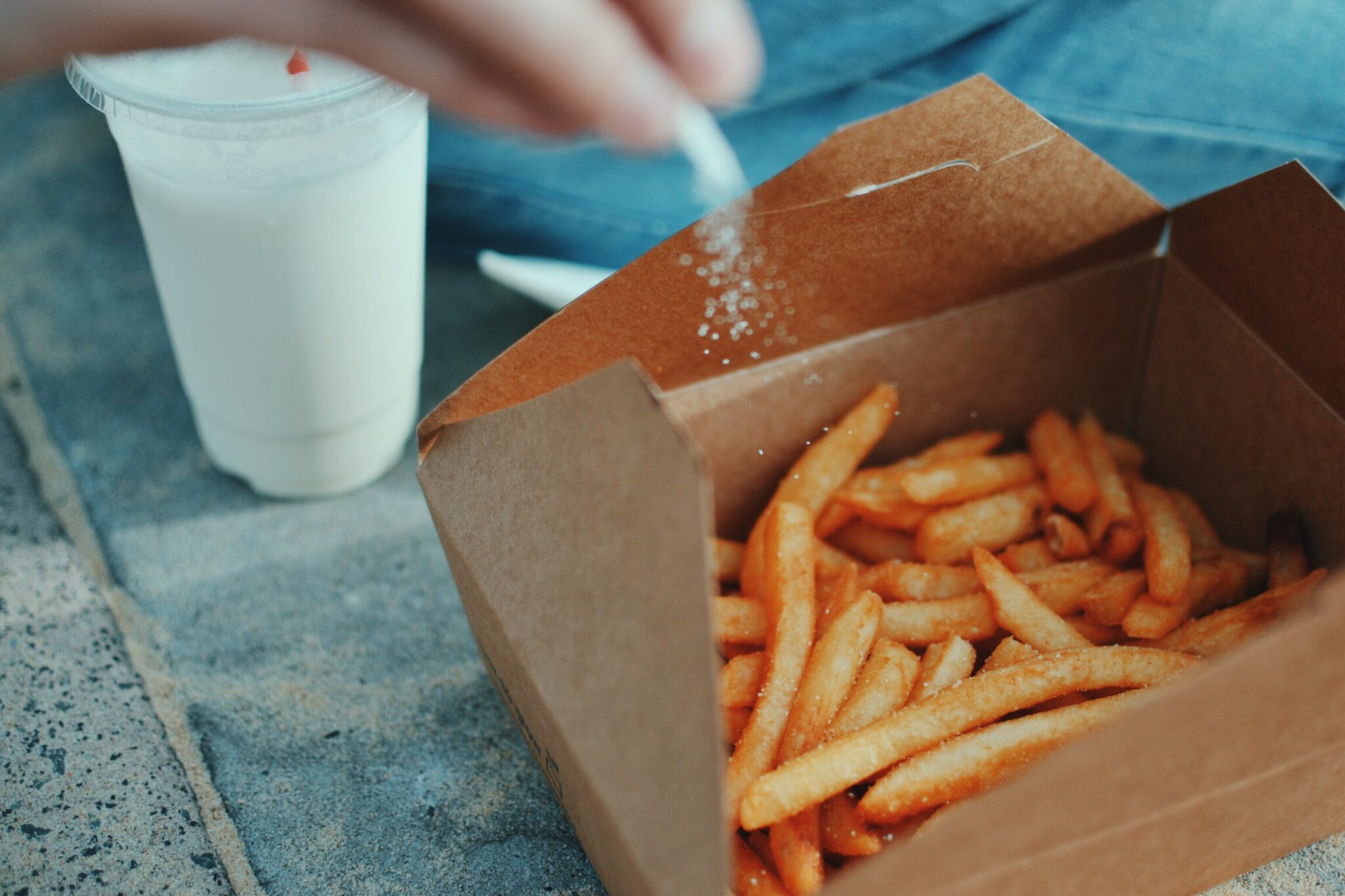 someone putting some salt on some chips in a brown takeaway box for the page collecting bank transfer payments as a takeaway